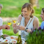 Three generations of women enjoy glasses of wine and food at an outdoor picnic setting