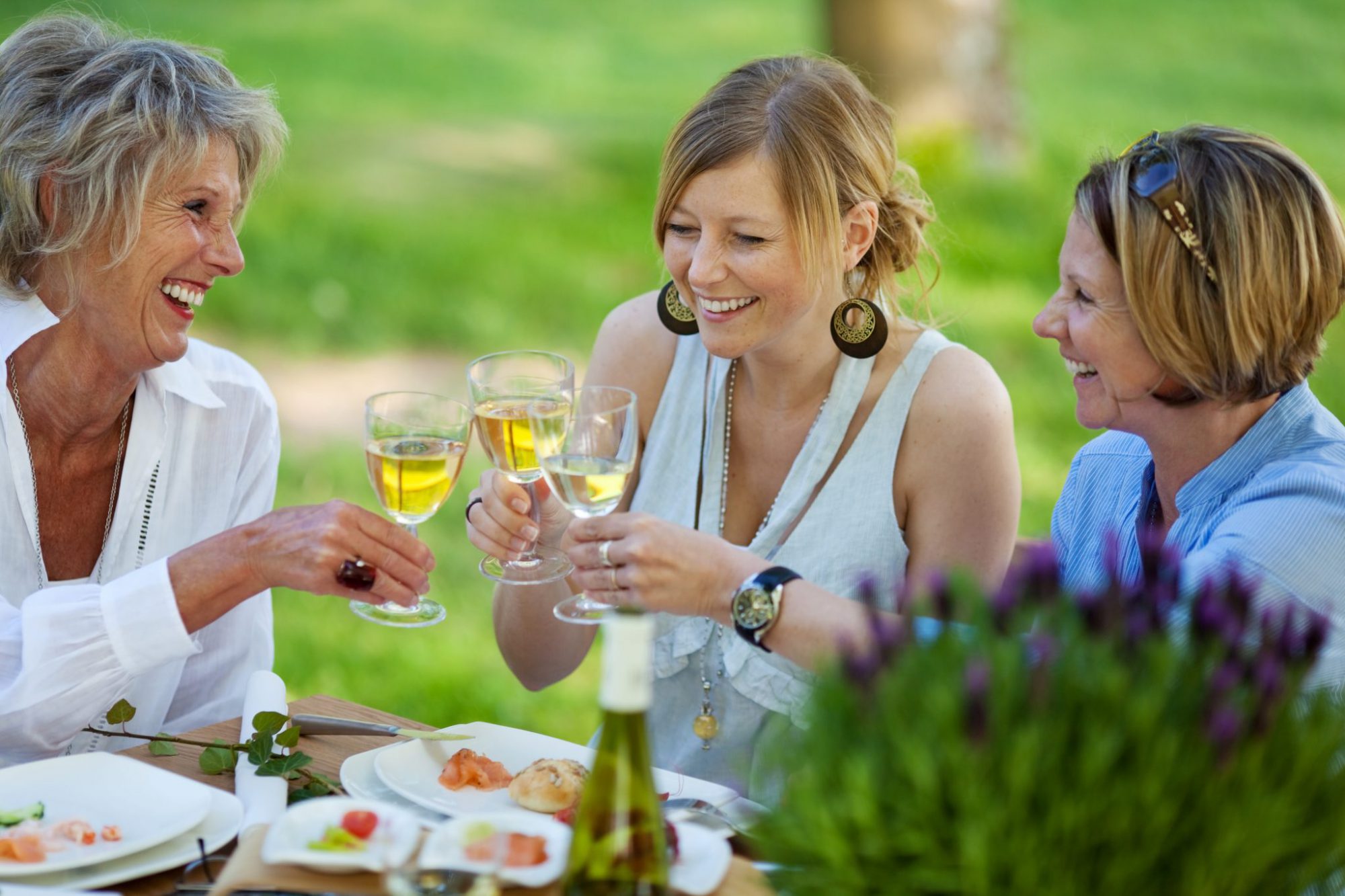 Three generations of women enjoy glasses of wine and food at an outdoor picnic setting
